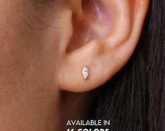 May include: A close-up of a person's ear with a small, marquise-shaped diamond earring. The earring is set in gold and is available in 16 colors. AVAILABLE IN 16 COLORS