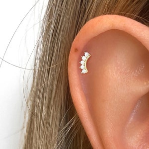 May include: A gold ear piercing with a crescent moon design featuring five small clear cubic zirconia stones.