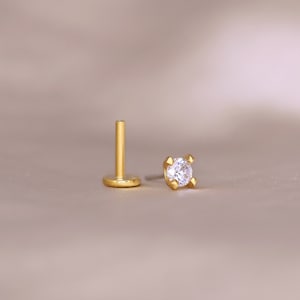 May include: A gold stud earring with a clear round gemstone.