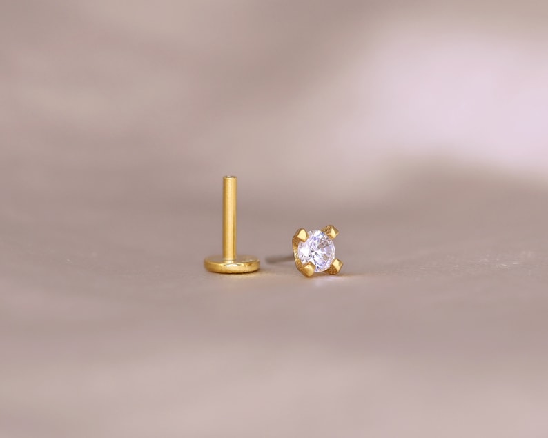 May include: A gold stud earring with a clear round gemstone.