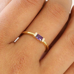 May include: A gold ring with a purple rectangular gemstone and two smaller clear gemstones on either side.