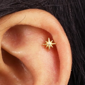 Könnte beinhalten: Goldener Stern-Ohrstecker für ein Helix-Piercing. Der Ohrstecker ist klein und zart, mit einem schlichten Design.