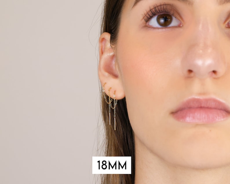 Puede incluir: Primer plano de la oreja de una persona con un pendiente de cadena dorada con tres cadenas colgantes. El pendiente mide 18 mm de largo.