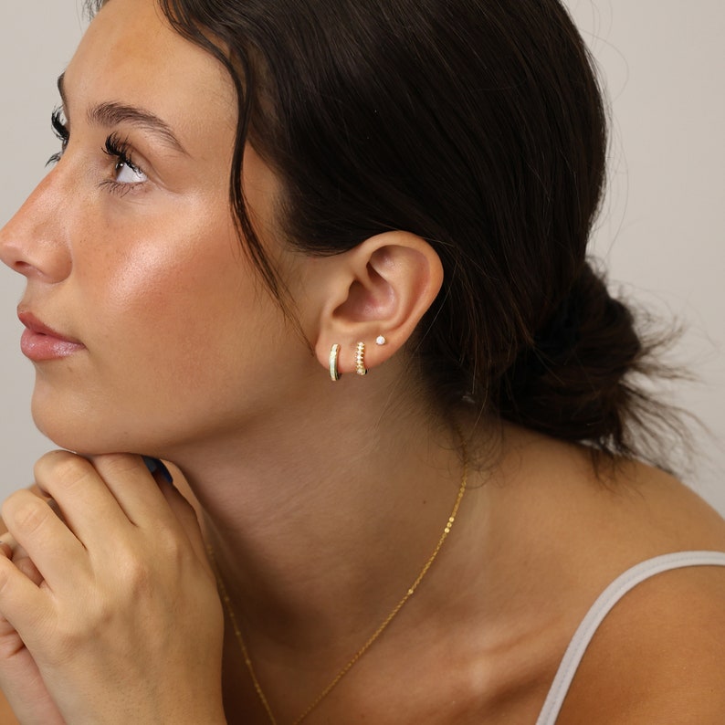 May include: A woman wearing gold hoop earrings with a small gold stud earring in her other ear.