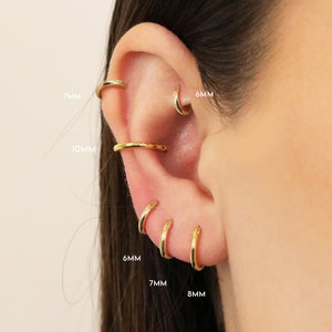 May include: Close-up of a person's ear with multiple gold hoop earrings in different sizes: 6mm, 7mm, 8mm, and 10mm.