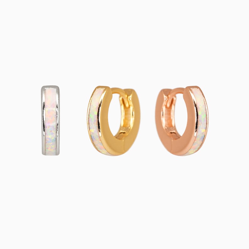 May include: Three hoop earrings with a white opal inlay. The hoops are available in silver, gold, and rose gold.