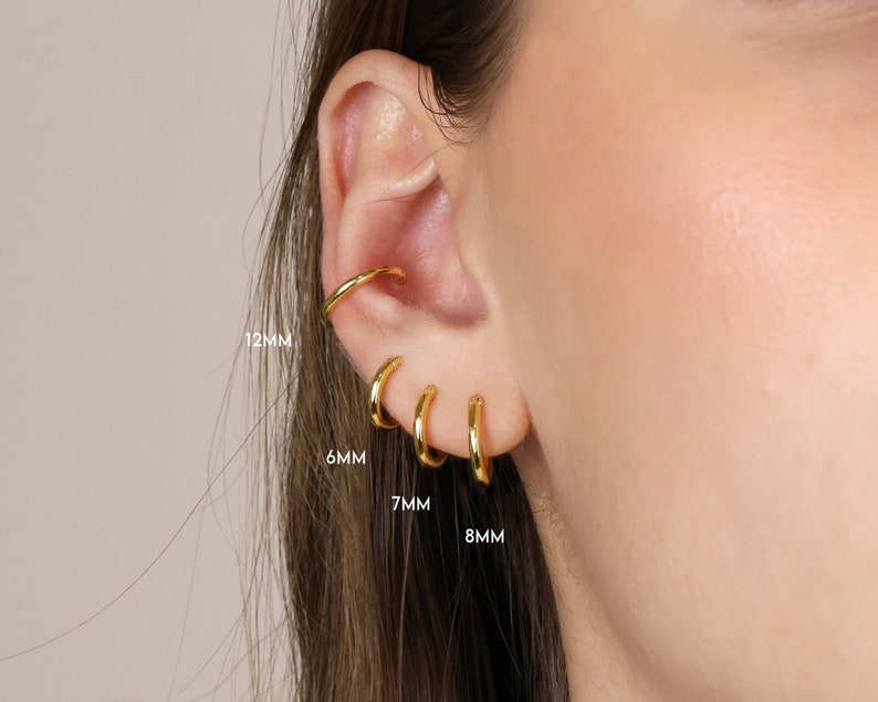 May include: Four gold hoop earrings in different sizes: 6mm, 7mm, 8mm, and 12mm. The earrings are shown on a person's ear.