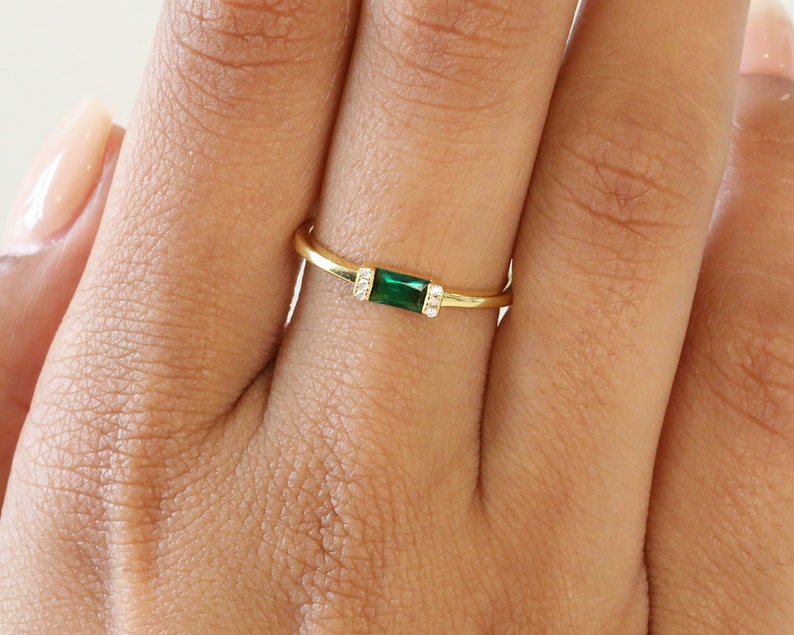 May include: A gold ring with a green emerald-cut gemstone and small clear stones on the band.