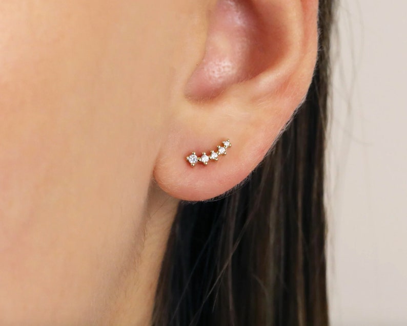 Pu&ograve; includere: Un orecchino a lobo in oro con cinque piccole pietre di zircone cubico trasparenti incastonate in una linea curva.