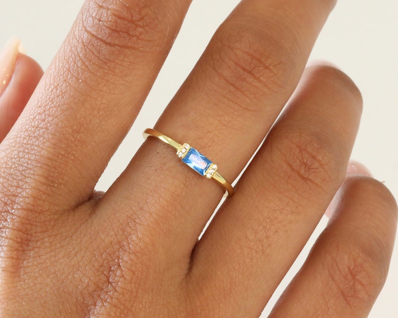 May include: A gold ring with a light blue rectangular gemstone and small clear gemstones on either side.