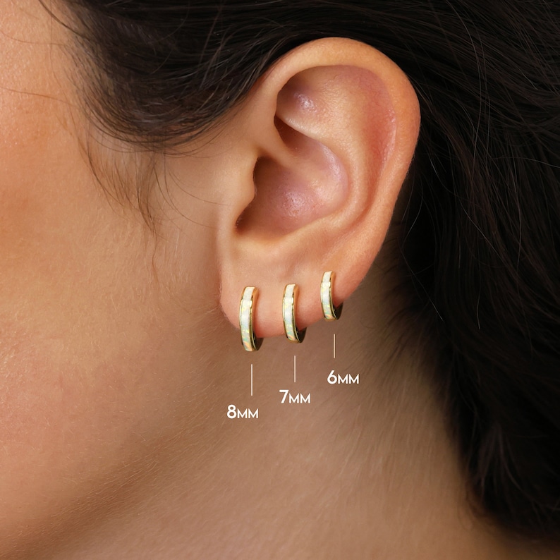 May include: Three gold hoop earrings with white opal inlay. The earrings are shown on a model's ear and are labeled with their sizes: 8mm, 7mm, and 6mm.