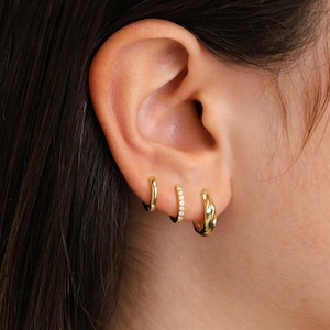 May include: A close-up of a person's ear with three gold hoop earrings. The earrings are different sizes and styles, with one featuring a row of small diamonds.