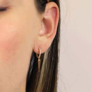 May include: Gold hoop earrings with a small diamond-encrusted band and a dangling pointed spike.