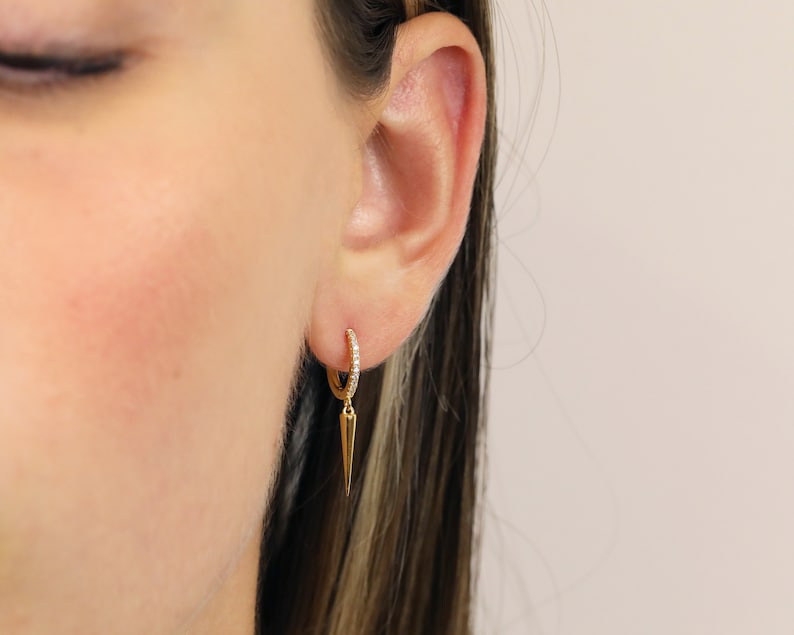 May include: Gold hoop earrings with a small diamond-encrusted band and a dangling pointed spike.