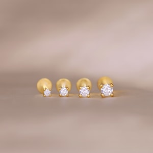 May include: Four gold-toned stud earrings with clear round gemstones. The earrings are arranged in a row from smallest to largest.