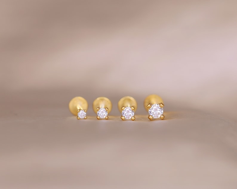 May include: Four gold-toned stud earrings with clear round gemstones. The earrings are arranged in a row from smallest to largest.