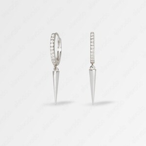 May include: A pair of silver hoop earrings with a small, pointed spike dangling from each hoop. The hoops are decorated with a row of small, clear cubic zirconia stones.