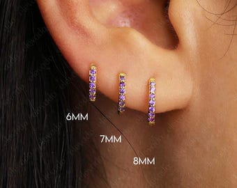 Könnte beinhalten: Drei goldene Creolen mit violetten Edelsteinen. Die Ohrringe haben einen Durchmesser von 6 mm, 7 mm und 8 mm.