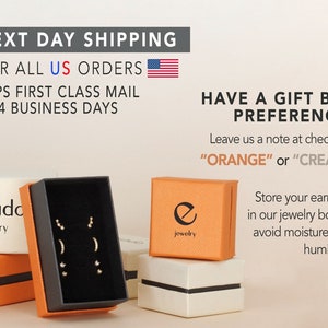 May include: Two small orange boxes with black lids and the text "elevado jewelry" and "e jewelry" on them. The boxes are sitting on a white surface. The box on the left is open and contains a set of earrings. The text "HAVE A GIFT BOX PREFERENCE? Leave us a note at checkout! "ORANGE" or "CREAM" " is visible on the right side of the image.