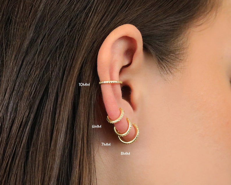 May include: Gold-colored hoop earrings and ear cuff with small, sparkling embellishments. The ear cuff is 10mm, and the hoops are 6mm, 7mm, and 8mm in diameter. The jewelry is displayed on an ear with dark brown hair.