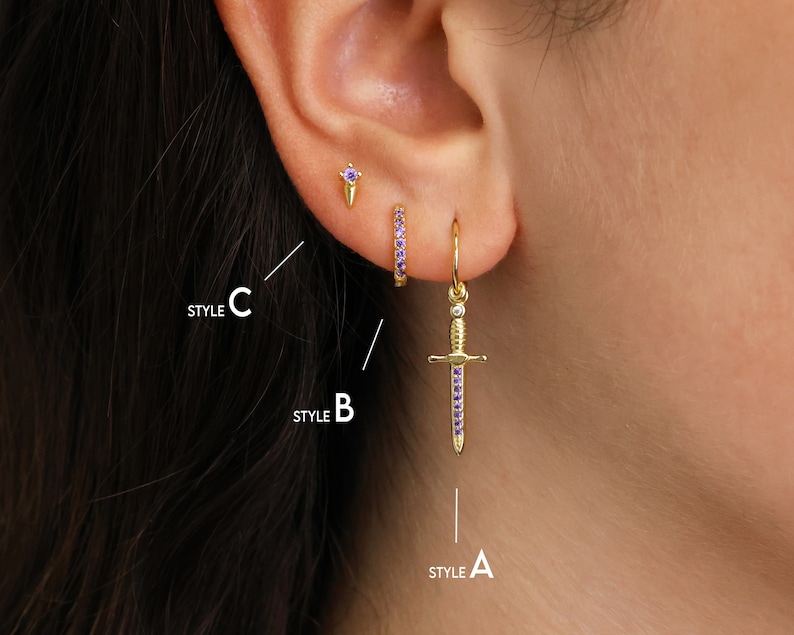 May include: Three different styles of earrings with purple gemstones. Style A is a dangling sword earring, Style B is a small hoop earring, and Style C is a small stud earring.
