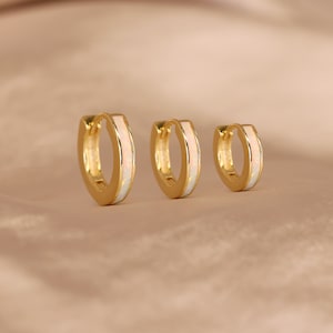 May include: Three gold hoop earrings with a white opal inlay. The earrings are different sizes.