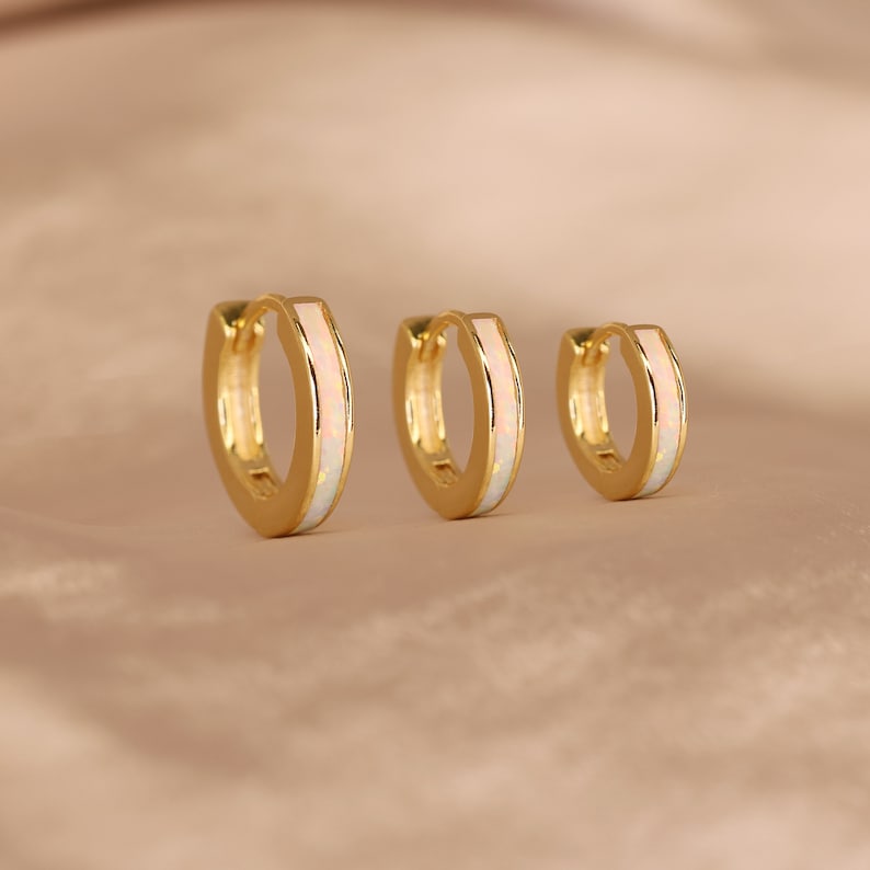 May include: Three gold hoop earrings with a white opal inlay. The earrings are different sizes.