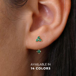 Peut inclure: Une paire de petites boucles d'oreilles en or avec des pierres précieuses vertes. Les boucles d'oreilles ont la forme d'un triangle avec trois pierres précieuses dans chaque triangle. Les boucles d'oreilles sont disponibles en 14 couleurs. DISPONIBLE EN 14 COULEURS