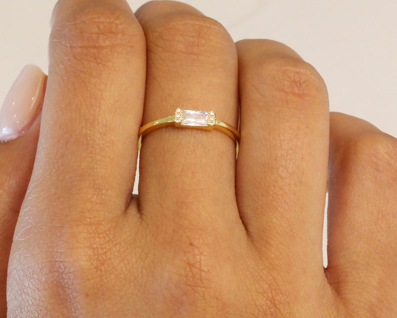 May include: A gold ring with a rectangular clear stone and two smaller clear stones on either side.