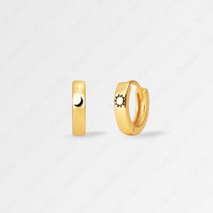 May include: A pair of gold hoop earrings with a small sun and moon design. The earrings are about 1 inch in diameter.
