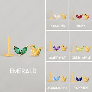 Może przedstawiać: Sześć par złotych kolczyk&oacute;w z r&oacute;żnokolorowymi kamieniami szlachetnymi. Każdy kolczyk ma parę kamieni szlachetnych w kształcie markizy osadzonych w złotej liści. Kamienie szlachetne to: diament, rubin, szmaragd, ametyst, zielone jabłko, akwamaryn i szafir.