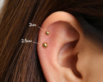 May include: Close-up of a person's ear with two gold stud earrings. The top earring is 2mm and the bottom earring is 2.5mm.
