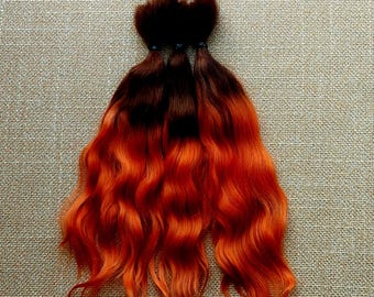 May include: Three bundles of wavy human hair extensions. The hair is dark brown at the roots and fades to a bright orange-red colour.
