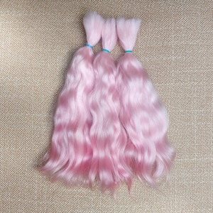 May include: Three bundles of light pink doll hair, each secured with a small blue elastic band. The wavy hair has a soft, pastel color and a silky texture, perfect for doll customization or crafting projects.