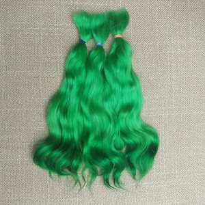 May include: Three bundles of bright green, wavy hair extensions. Each bundle is secured with a small, colorful elastic band. The hair has a vibrant, saturated color and a soft, flowing texture, perfect for cosplay or costume use.