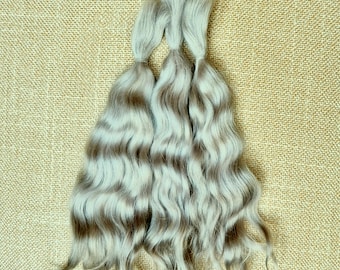 May include: Three bundles of wavy, light ash-blonde hair extensions with subtle darker brown lowlights. Each bundle is secured at the top with a small band, allowing the long, wavy strands to flow downward in a natural, layered arrangement.