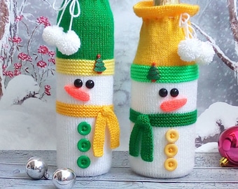 Può includere: Due copribottiglie a forma di pupazzo di neve di lana, uno verde e uno giallo, con pompon bianchi e occhi neri. Il testo sull'immagine dice "Вязаные игрушки Светлана Зайцева".