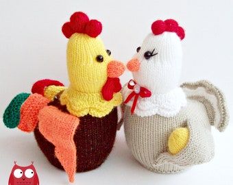 Può includere: Due galline di peluche a maglia, una gialla e marrone con una coda arancione, l'altra bianca e grigia con un fiocco rosso. Le galline si guardano.