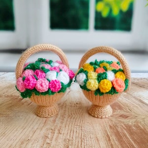 May include: Two knitted baskets filled with crocheted flowers. One basket has pink and white flowers, the other has yellow and orange flowers.