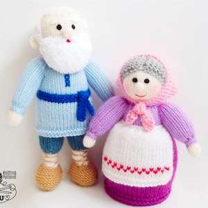 May include: Two knitted dolls: a man and a woman. The man doll wears a light blue tunic with a blue belt, blue pants, and tan shoes. The woman doll wears a purple sweater, a white apron with red accents, and a pink headscarf. The dolls have white hair and smiling faces.