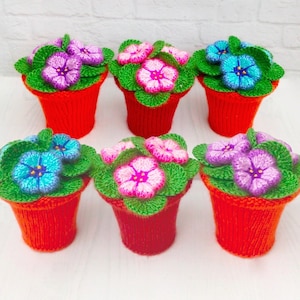 May include: Six crocheted flower pots with different coloured flowers. The pots are all red and the flowers are pink, blue, and purple.