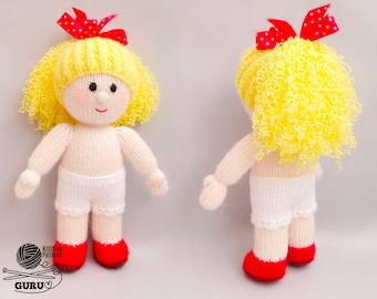 Può includere: Una bambola di lana con capelli ricci gialli, un fiocco rosso e vestiti bianchi. La bambola è in piedi su una superficie bianca.