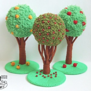 May include: Three crocheted trees with green foliage and brown trunks. The trees are decorated with red and yellow beads, resembling apples and oranges. The trees are standing on green bases.