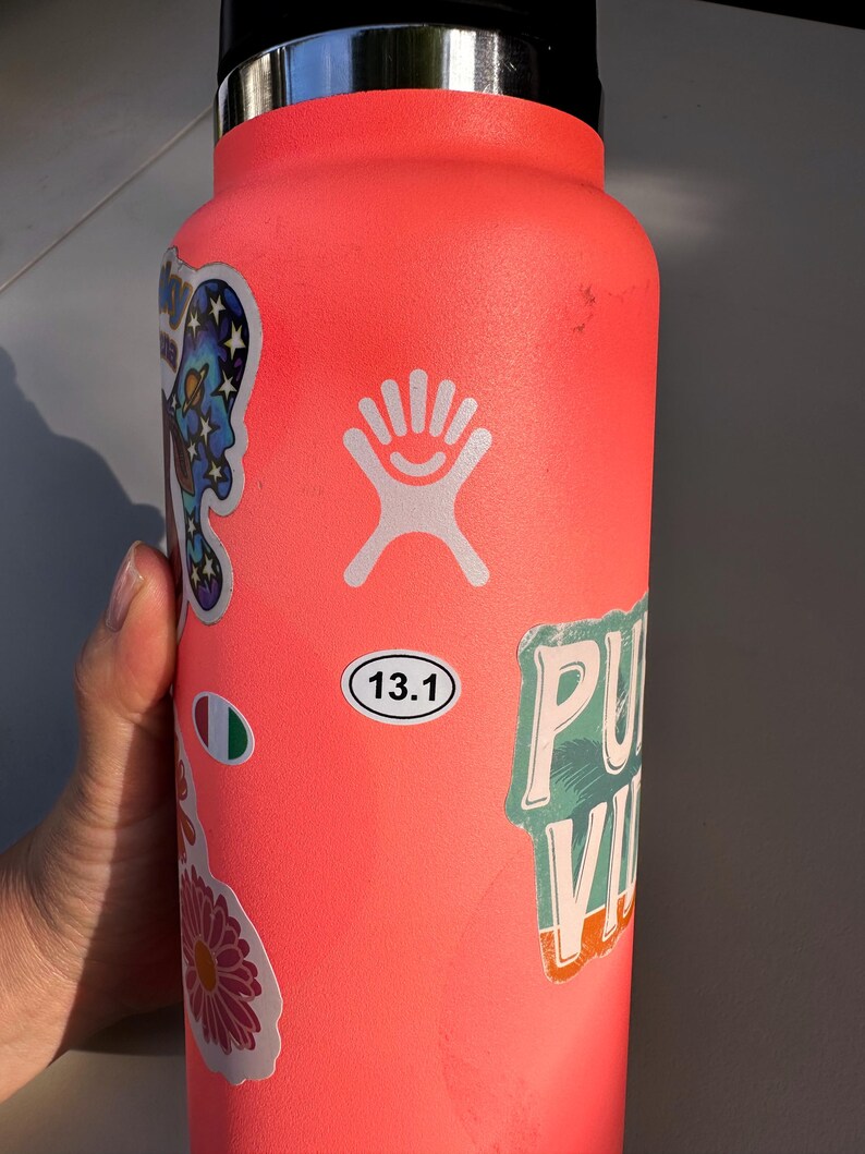 May include: A bright pink reusable water bottle with a white Hydro Flask logo and various stickers, including a sticker with the text "13.1" and a sticker with the text "PU" and "VI".