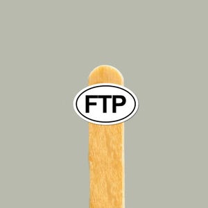 May include: A small oval sticker featuring the black text FTP centered on a white background with a thin black border, applied to the top portion of a light brown wooden craft stick with a rounded end, presented against a solid gray background.