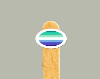 Puede incluir: Un palito de madera para helado con una pegatina redonda que presenta un diseño a rayas verde, verde claro, azul y morado.