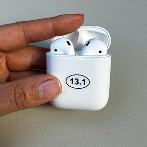 May include: White wireless earbuds in a white charging case with a sticker that says "13.1" on the front.