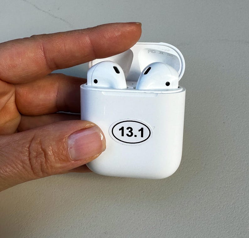 May include: White wireless earbuds in a white charging case with a sticker that says "13.1" on the front.