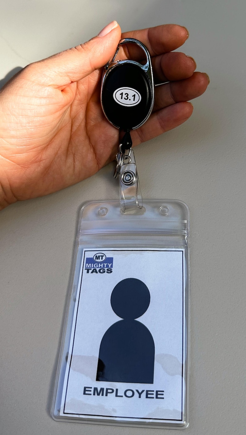 May include: A clear plastic badge holder with a black and white employee badge inside. The badge has a silhouette of a person and the text "EMPLOYEE". The badge holder is attached to a retractable badge reel with a black oval and the number "13.1" printed on it.