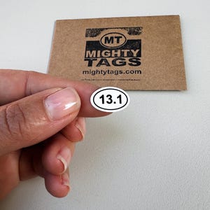 May include: White oval sticker with black text "13.1" on a white background. The sticker is being held by a hand.